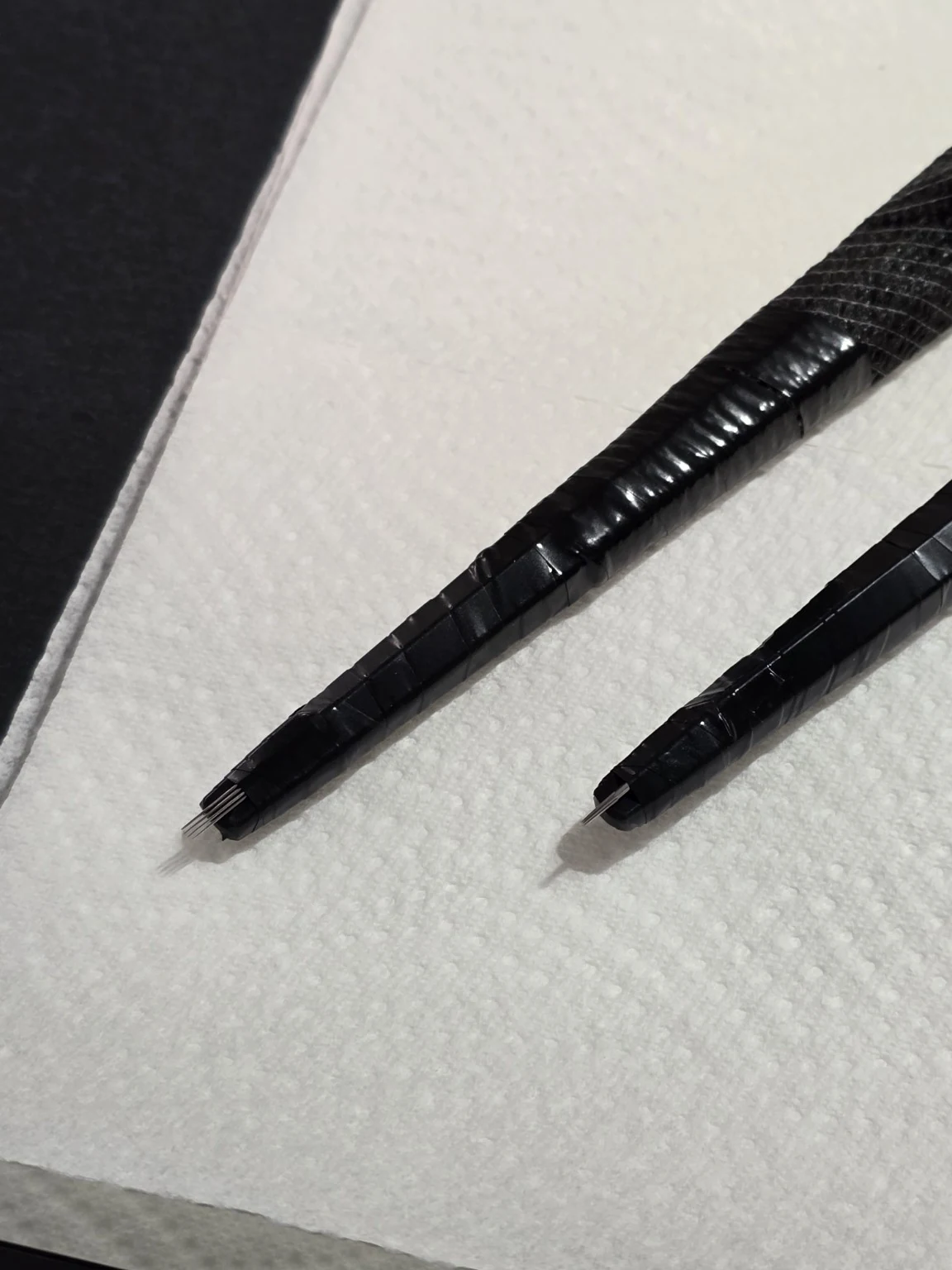 Two black hand-held tattoo tools resting on a white work surface.