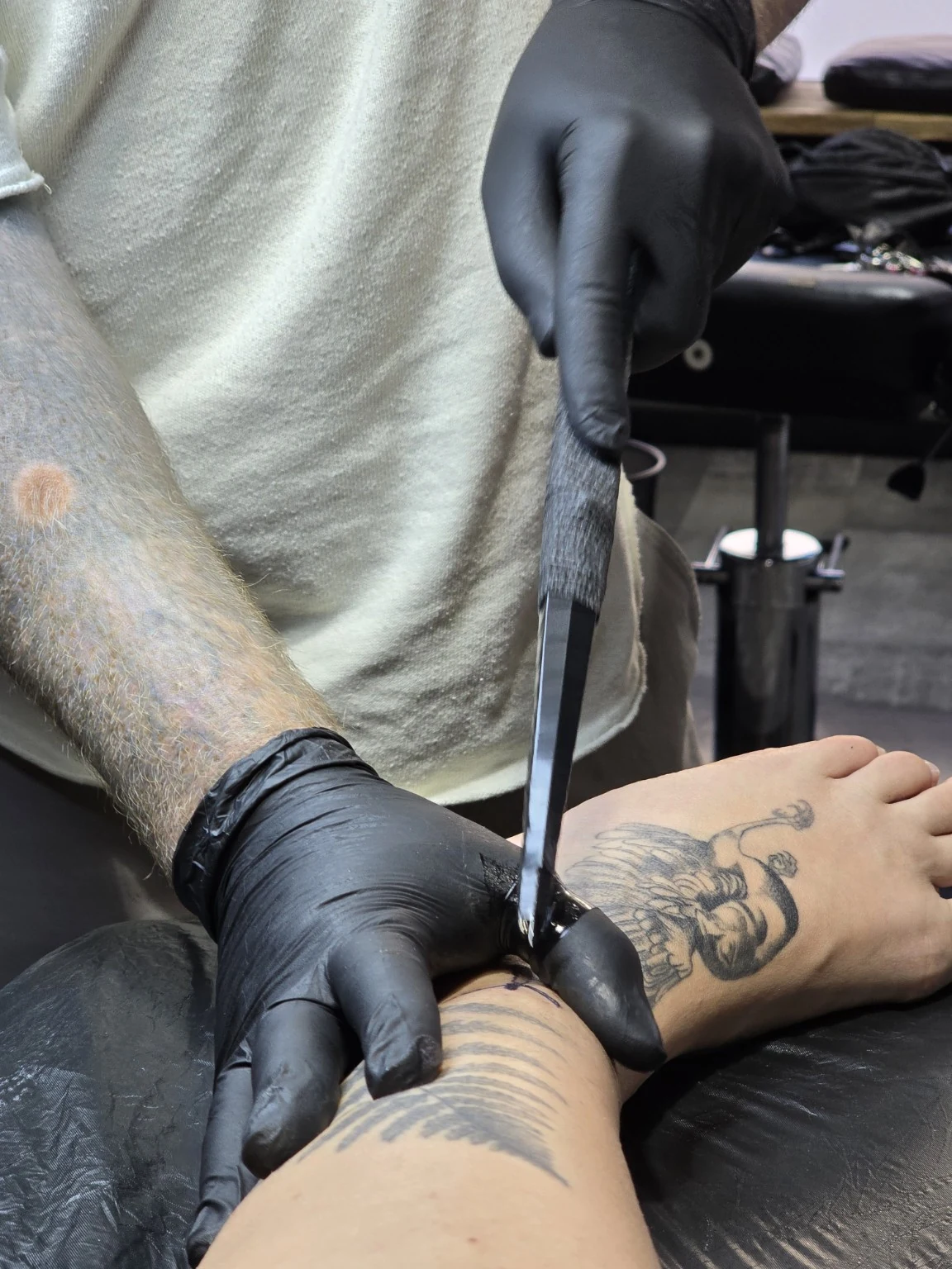 Wider view of a hand-held tattoo tool in use on a lower leg.